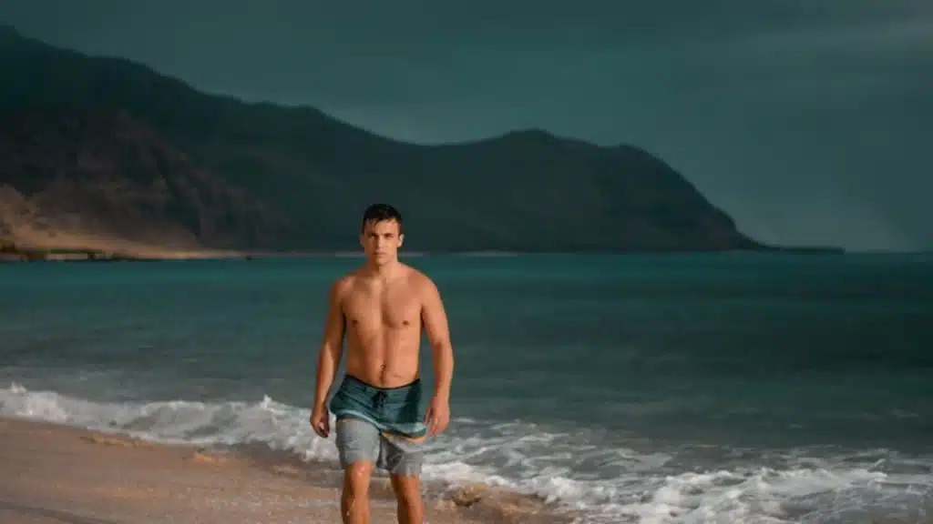 A shirtless man walking on the beach.