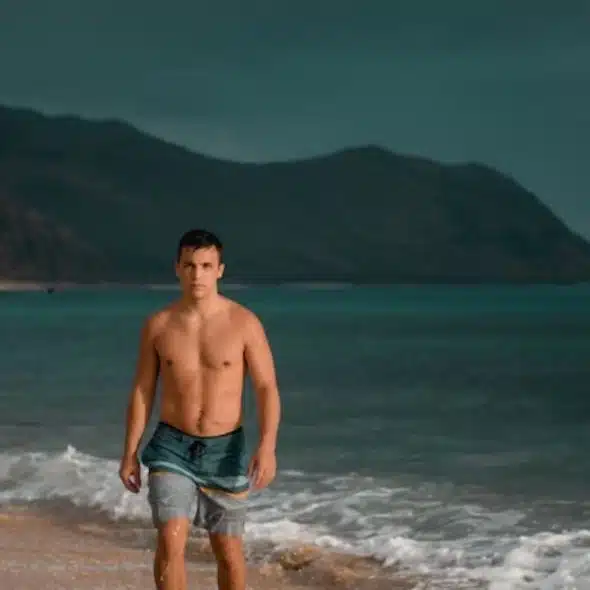 A shirtless man walking on the beach.