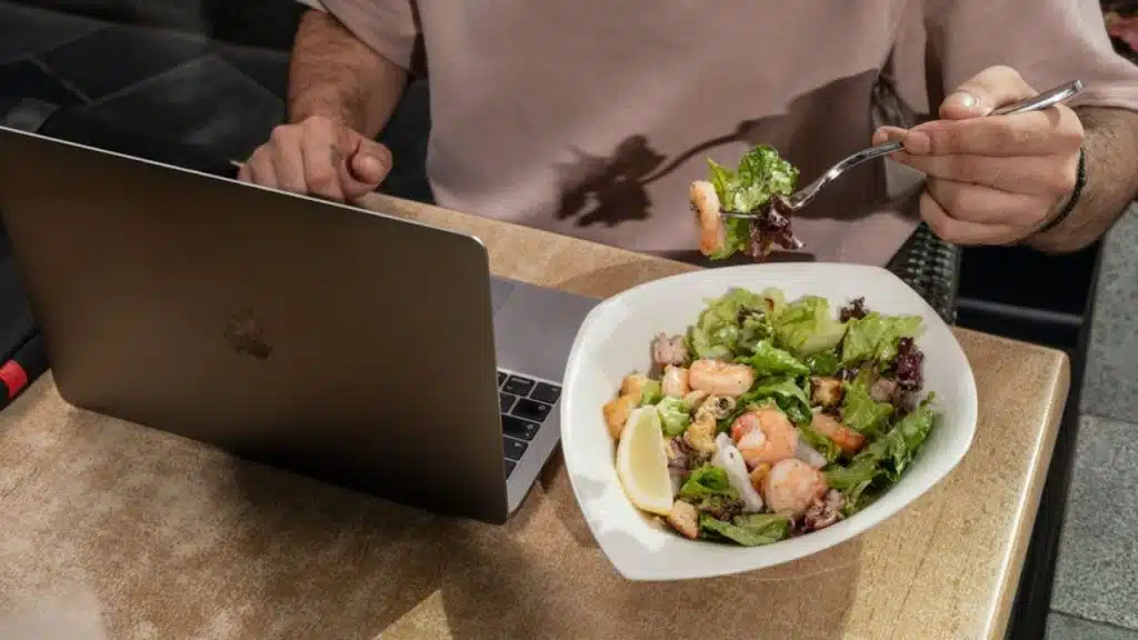 A man eating salad while working promotes healthy and sustainable weight loss.