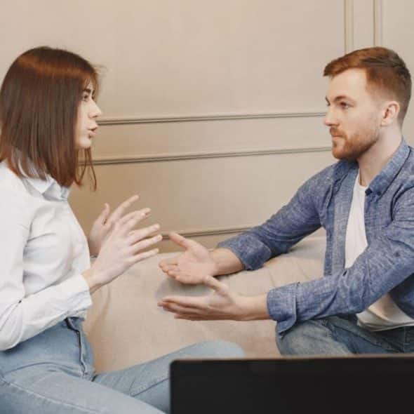 Couple sitting on the couch having an honest conversation in a quiet, respectful setting.