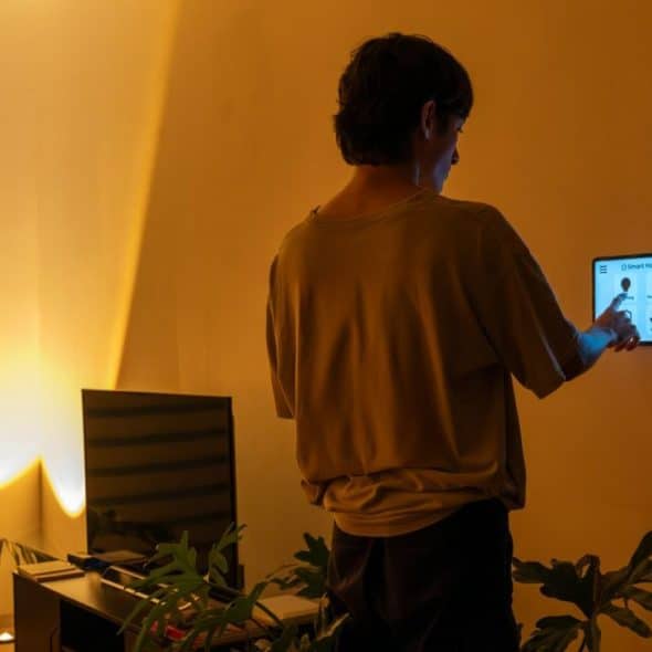 A person interacts with a wall-mounted smart home control panel in a dimly lit room.