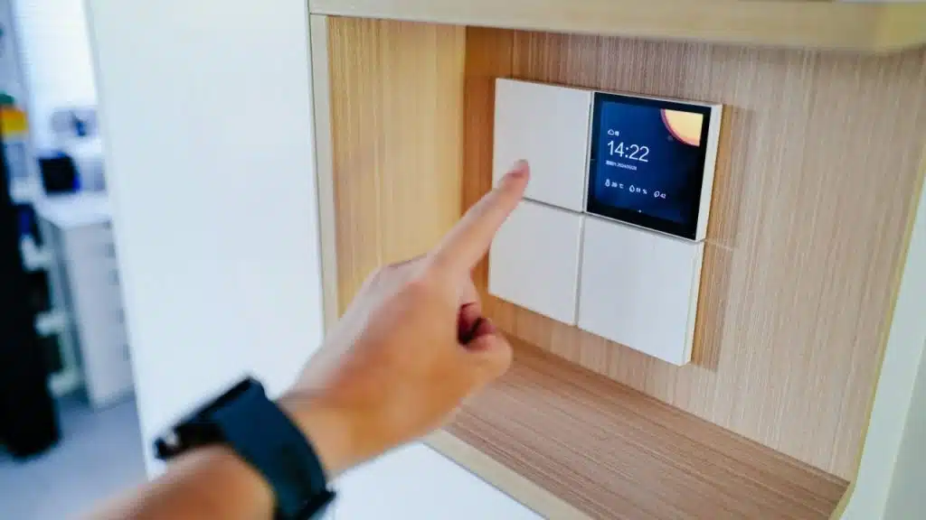 A person's finger touches a smart climate control panel with a digital display showing time and weather.