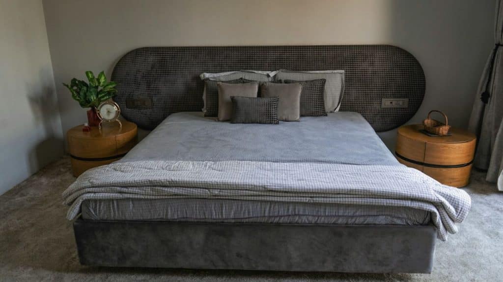 A bedroom features a bed with a gray headboard and bedding, flanked by two wooden nightstands.