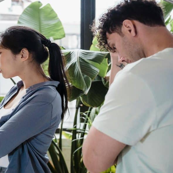 A man and woman stand facing away from each other in a room.