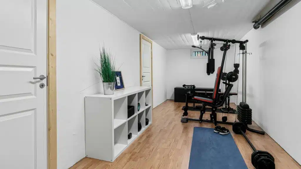 A small home gym features a multi-station weight machine, a blue mat, and a white storage unit.