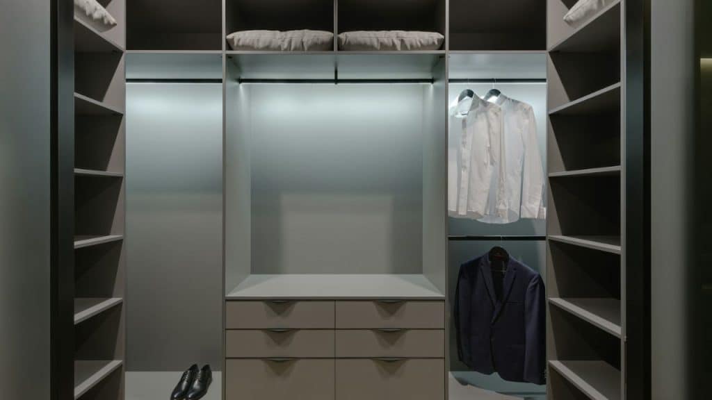 A custom walk-in closet with shelves, drawers, and hanging space for clothes, including a white shirt and a navy blazer.