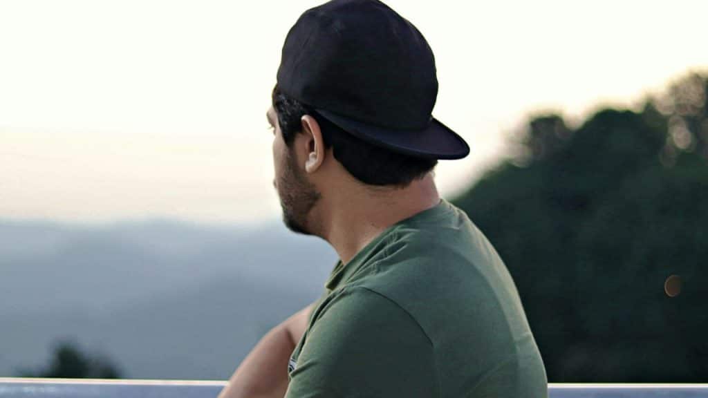 A man wearing a green shirt and a black baseball cap looks out over a landscape.