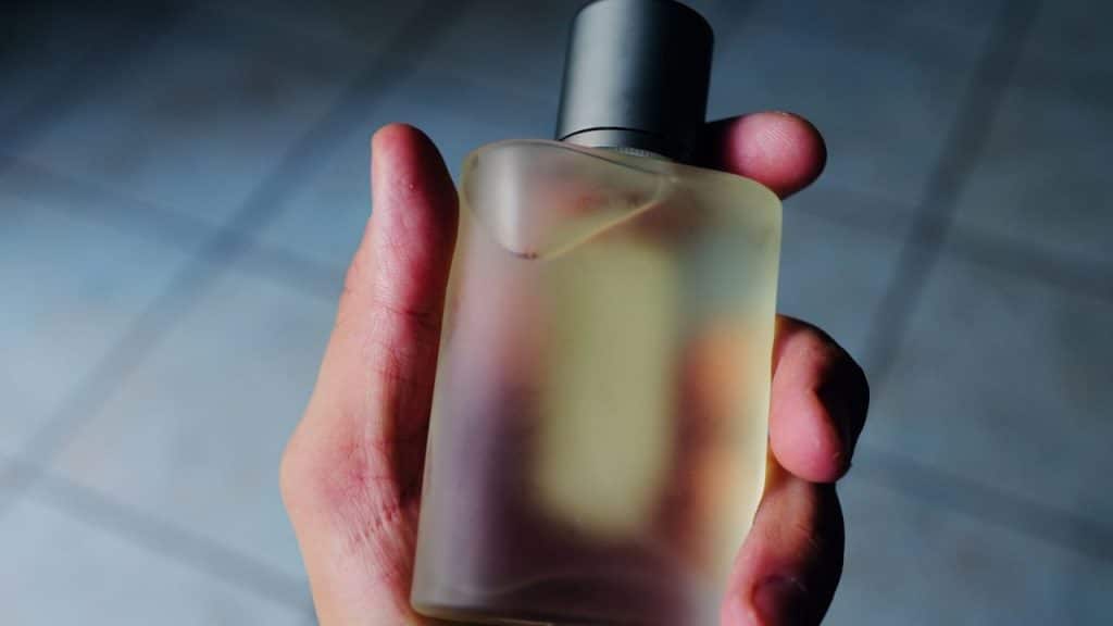 A hand holds a frosted glass perfume bottle with a dark cap.