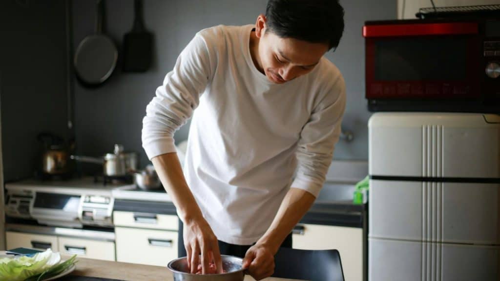 A man in a white shirt mixes ingredients in a bowl in a kitchen.