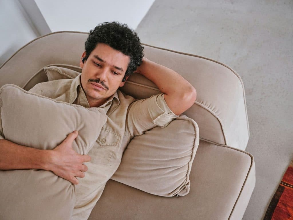 A man with his bluetooth earphones while on a sofa