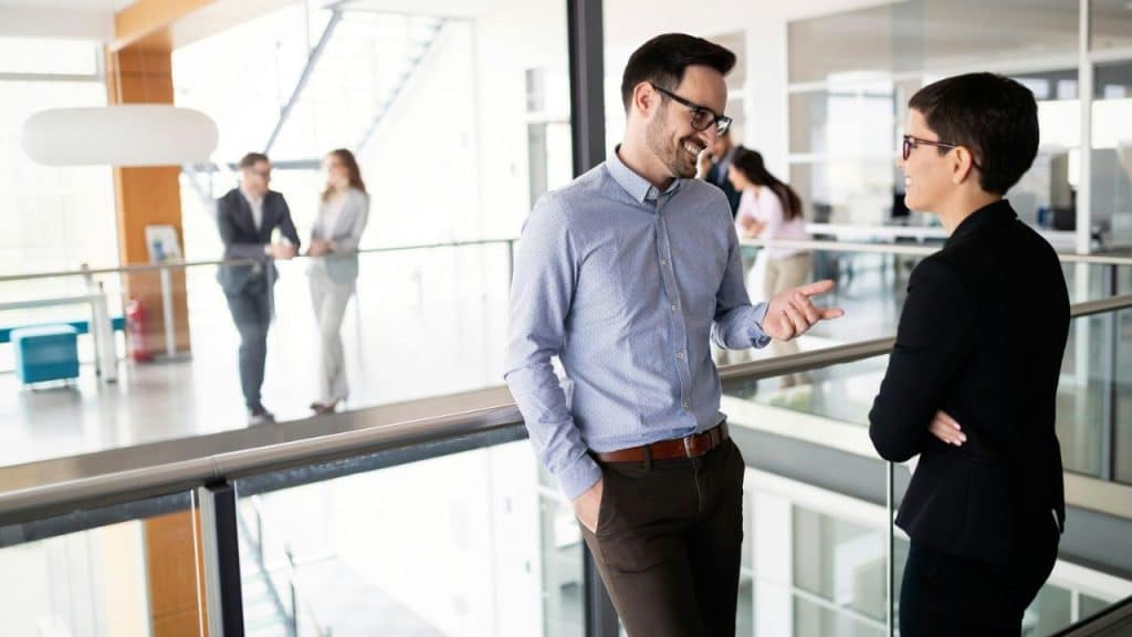 A man and a woman in business attire converse in a modern office space.