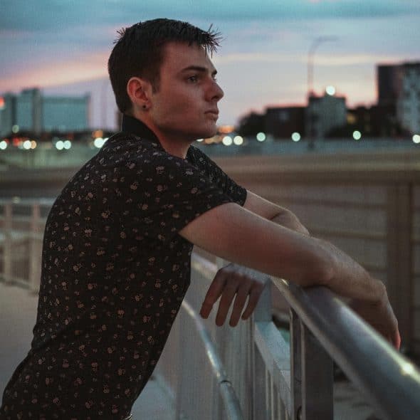 A man stands alone on a balcony at sunset, contemplating his future and relationship decisions