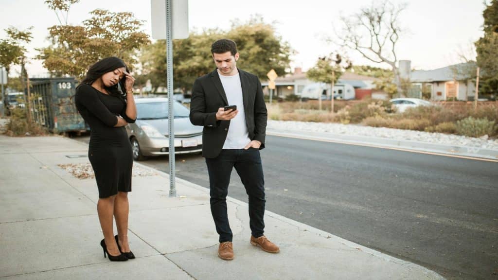A man looking at his phone and the woman appearing visibly upset, holding her head in one hand.