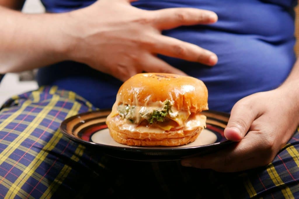 A man holding a burger and his tummy.