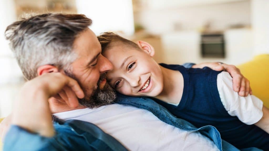 A father and son sitting indoors while smiling.