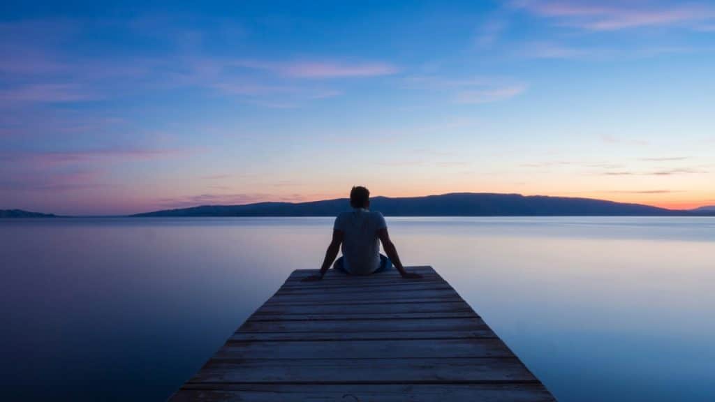 A man sitting on a dock at dusk.