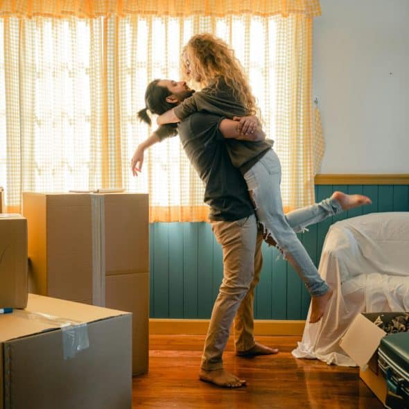 A happy couple embraces in a sunlit room surrounded by moving boxes
