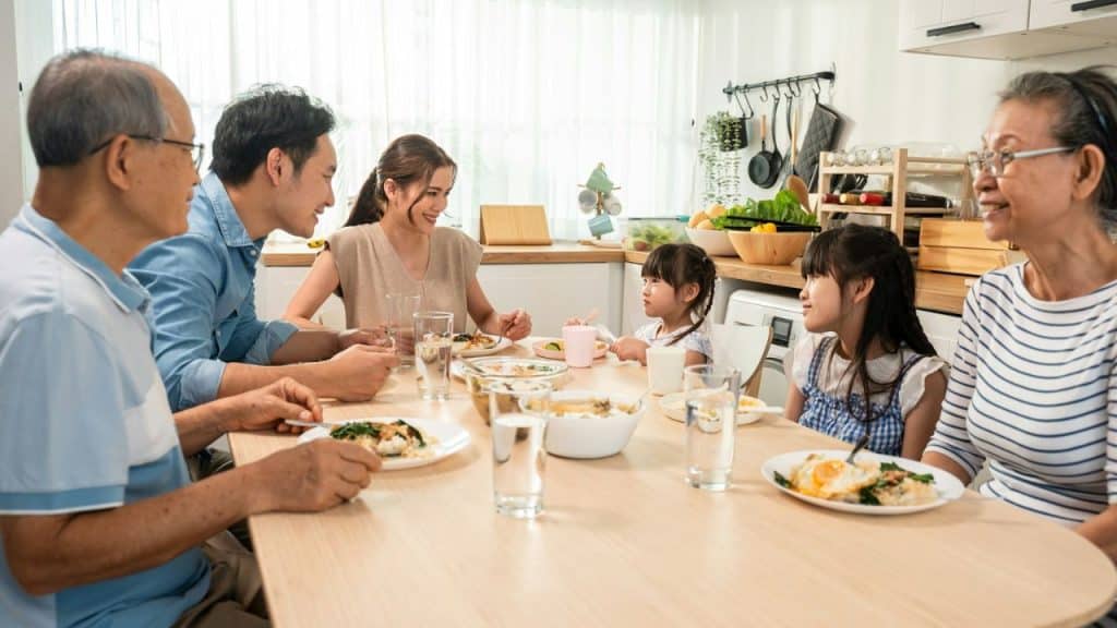 A multi-generational Asian family is gathered around a table, sharing a meal.