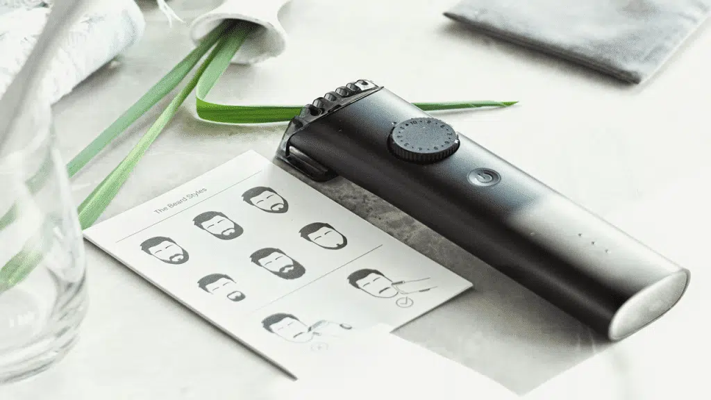 A black electric beard trimmer is placed on a countertop next to a grooming guide.