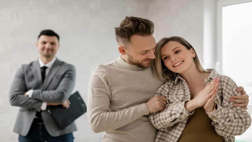 A happy couple stands closely together, smiling and embracing in a bright, empty room.