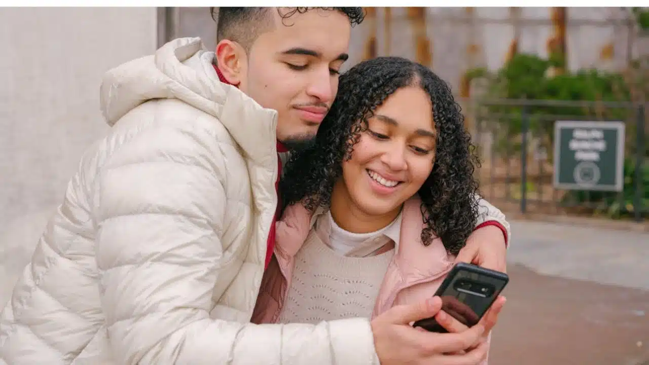 Man smiling as he scrolls through his phone in full view of his partner.