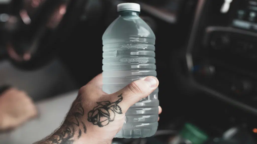 A tattooed hand is holding a clear plastic water bottle inside a car.