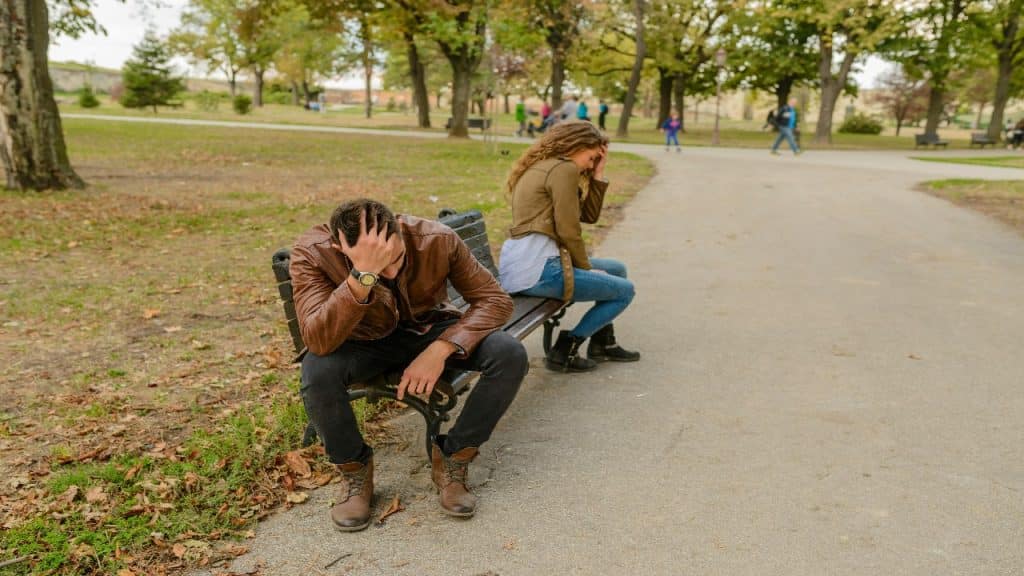 Couple sits quietly on a bench, struggling to open up to each other in a moment of vulnerability.