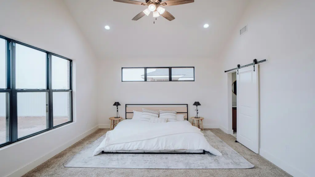 A minimalist bedroom features a low-profile bed with white bedding, matching pillows, and modern black lamps on wooden side tables.