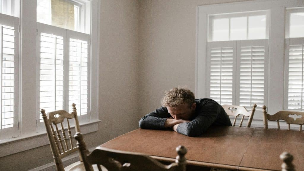 A stressed man sits alone at a kitchen table, silently dealing with emotional burnout.