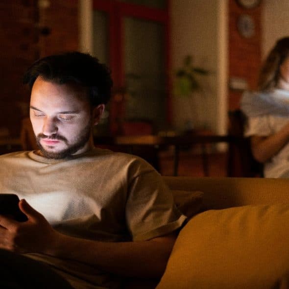 A couple sitting separately absorbed in their smartphones, creating visible emotional distance.