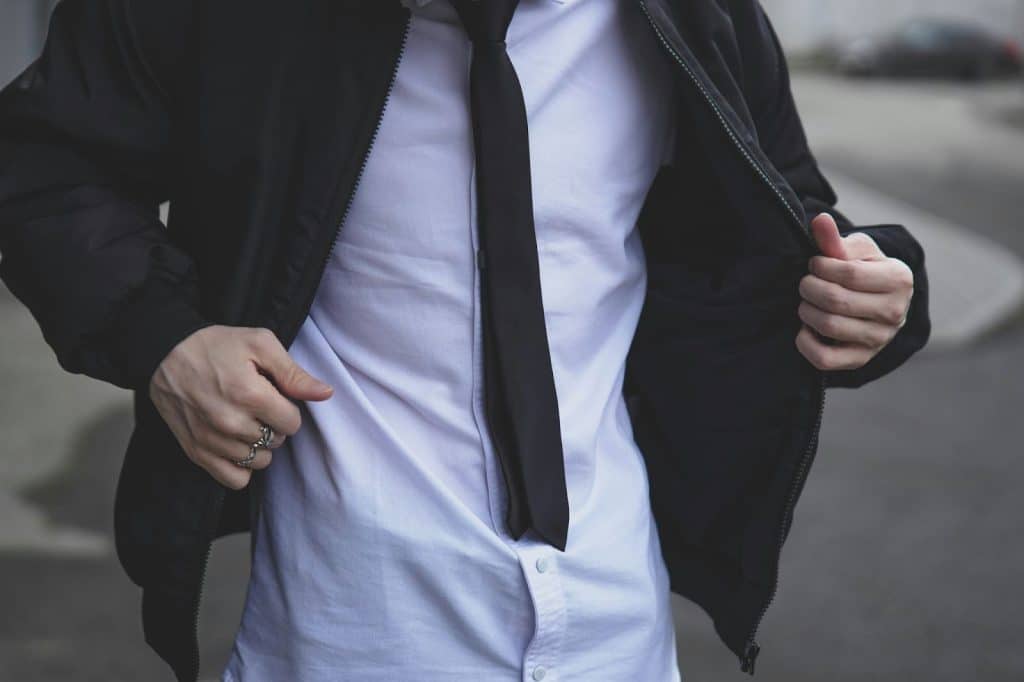 A man wearing a white polo, necktie, and a coat.
