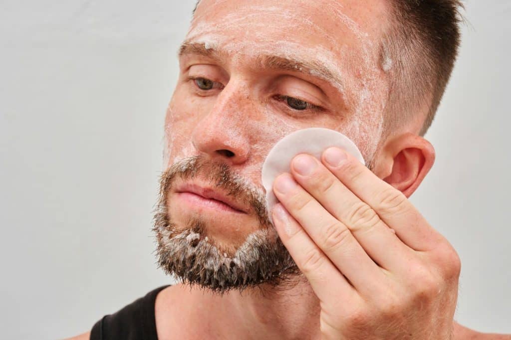 A man scrubbing his face with cotton and with his clean nails.