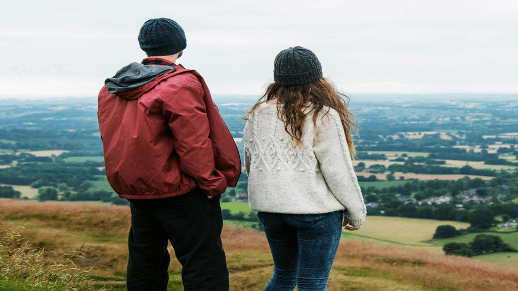 A couple stands on top of a hill and stares at the view.