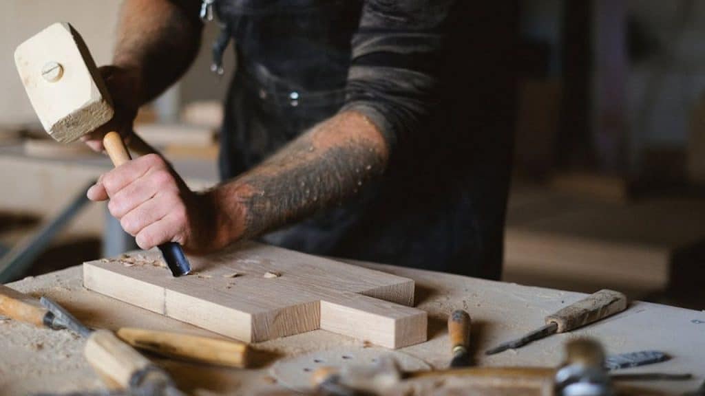 Man carving wood while others sketch or paint nearby.