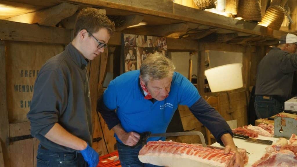 Older man teaching younger man to cut meat.
