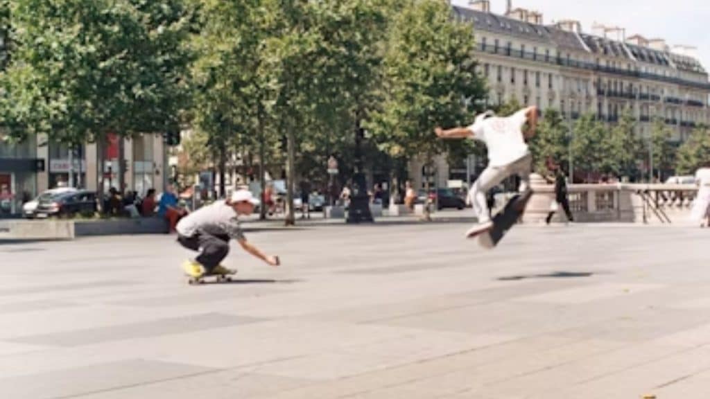 Adult men skating together through a city plaza.