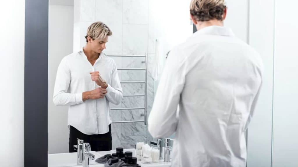 A man stands at a bathroom mirror with a serious expression.