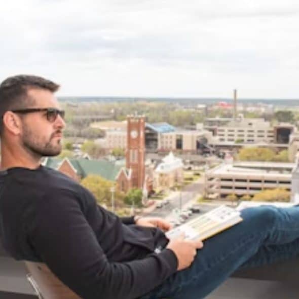 A man in his 30s sits alone on a rooftop, reflecting quietly.
