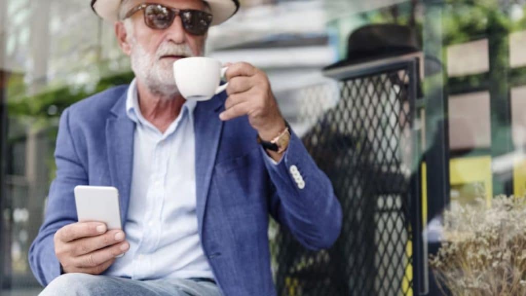 A stylish man in his 50s smiling confidently at an outdoor café.