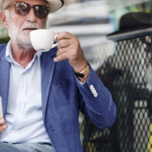 A stylish man in his 50s smiling confidently at an outdoor café.