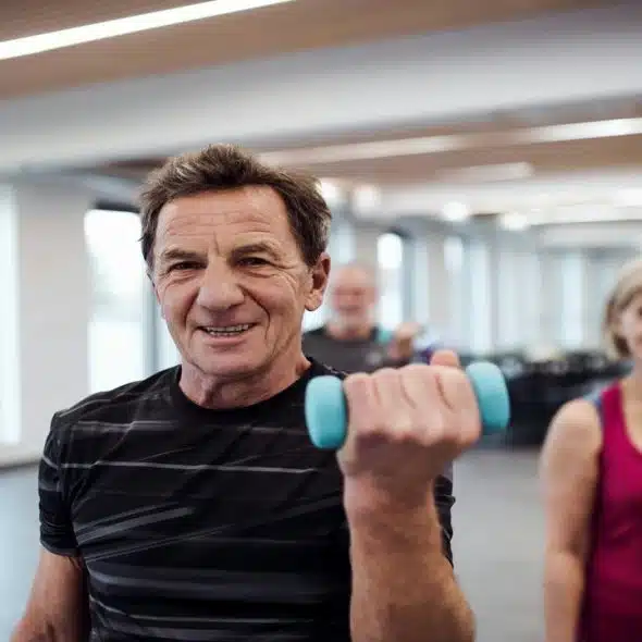 A group of older adults exercising with light dumbbells in a bright fitness studio.
