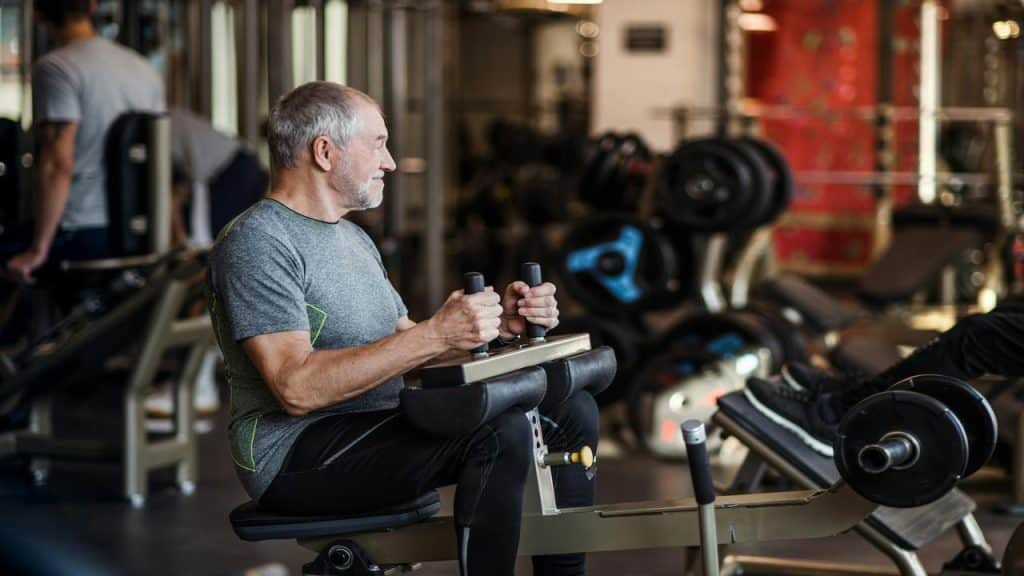 A senior man using a leg extension machine in a well-equipped gym, focusing on his workout.