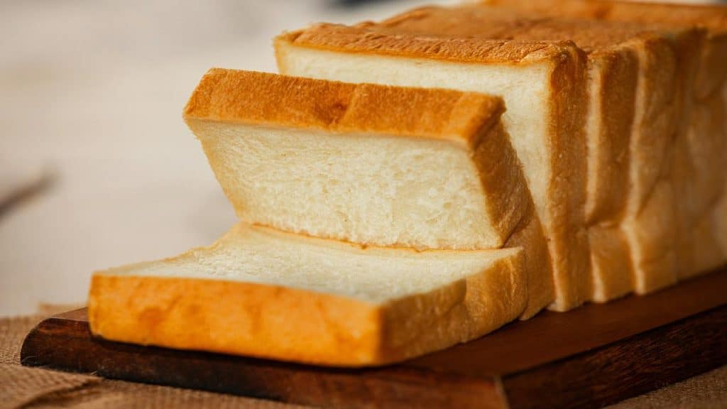 A loaf of sliced white bread on a wooden cutting board, with soft texture and golden-brown crust.