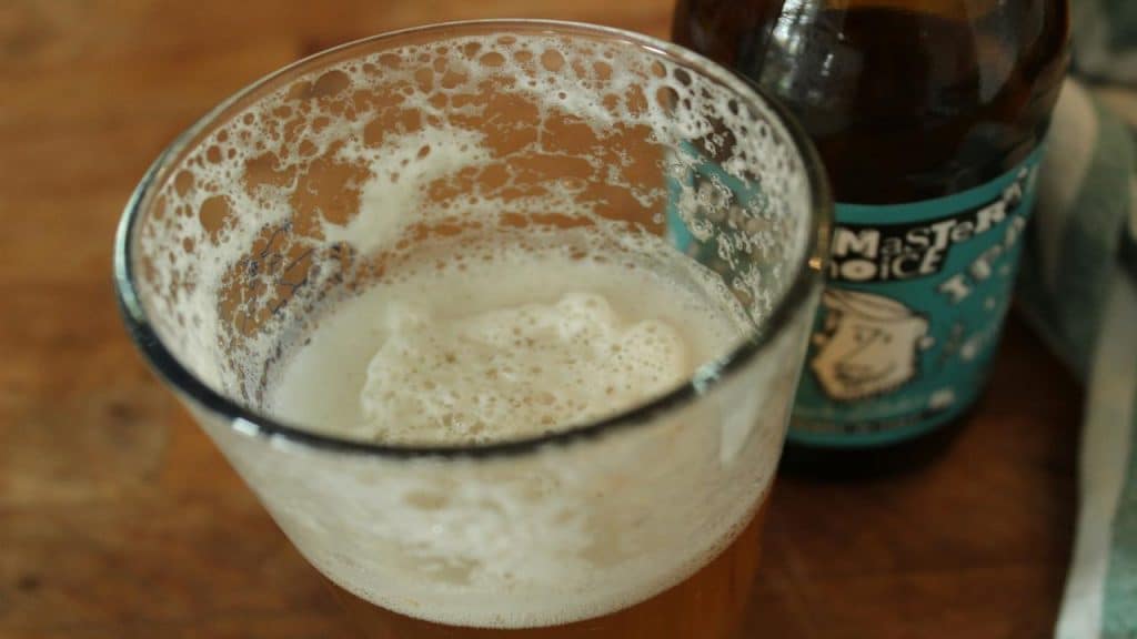 A partially filled glass of frothy beer next to a craft beer bottle.