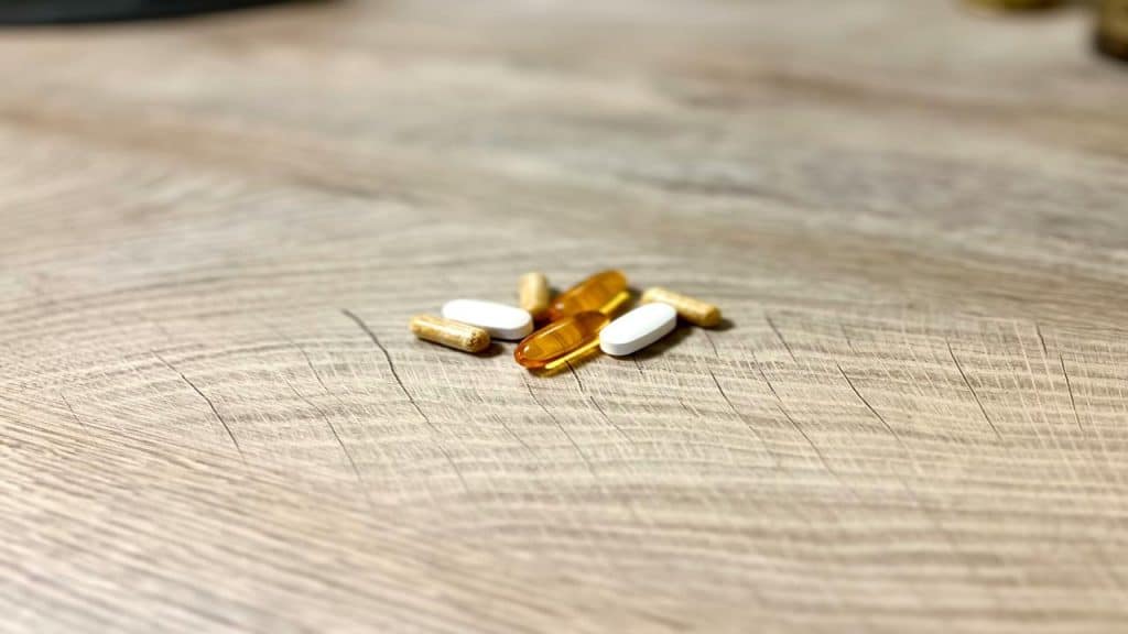 A small pile of assorted pills and capsules on a wooden surface.