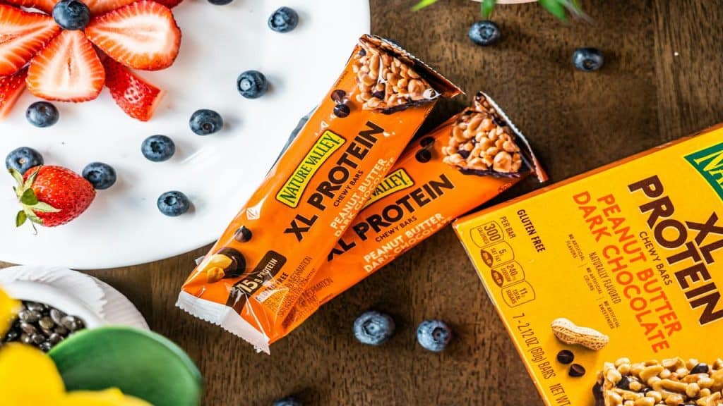 Nature Valley XL Protein bars in peanut butter dark chocolate flavor, surrounded by fresh strawberries and blueberries.