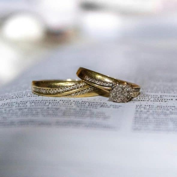 A pair of gold diamond rings resting on an open Bible.