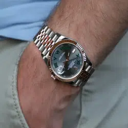 A two-tone Rolex Oyster Perpetual watch with green Roman numerals on a man's wrist.