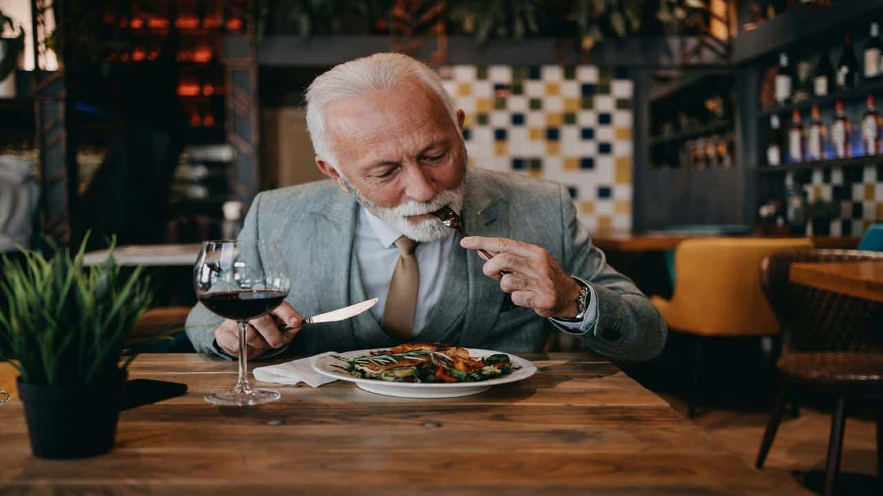 A well-dressed older man in a suit enjoys a gourmet meal with a glass of red wine in an elegant restaurant.