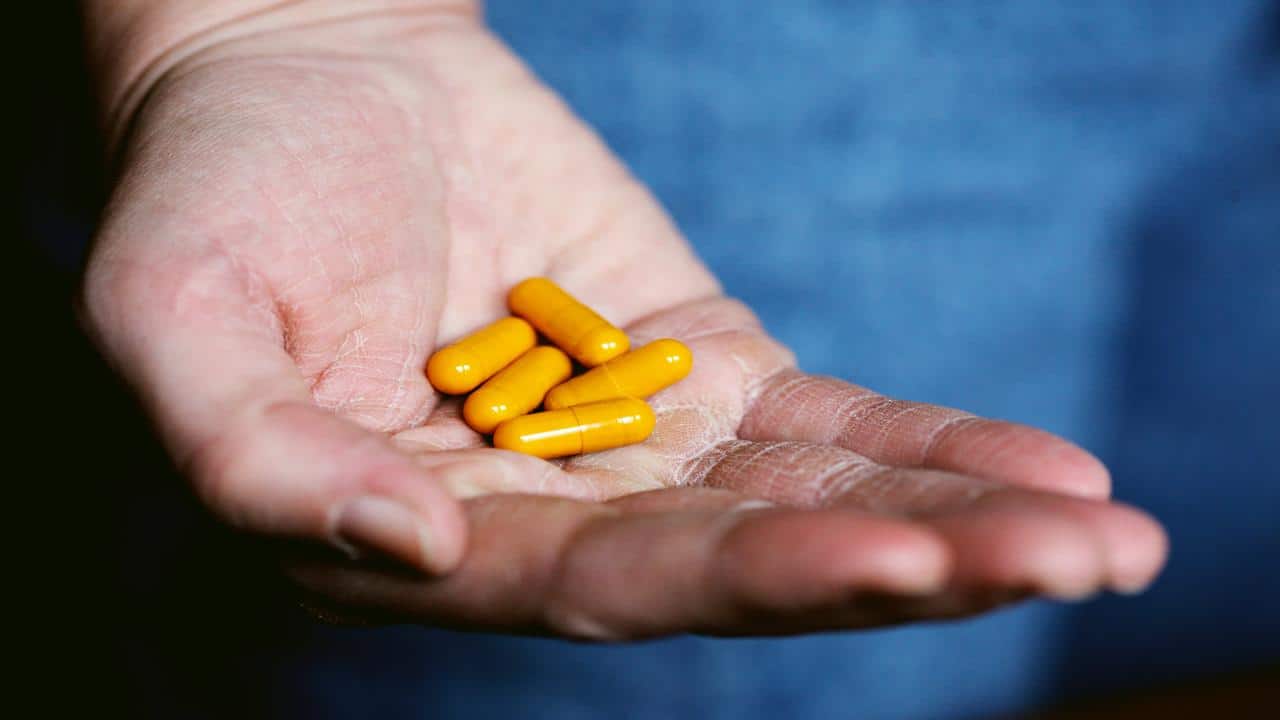 A hand holding several yellow capsule pills against a blurred blue background.